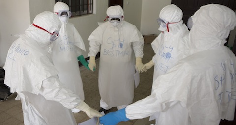Health workers wearing protective equipment pray at start of shift before entering Ebola treatment center in Liberia
