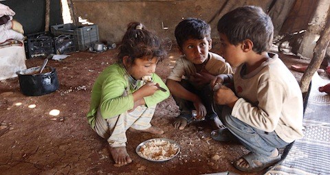 Internally displaced children eat inside a tent in Syria
